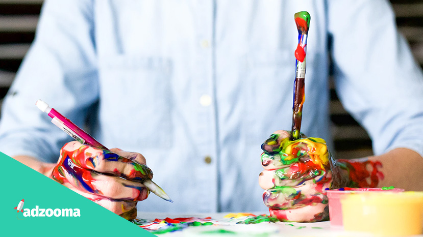 A creative man holding a pen and paintbrush covered in paint